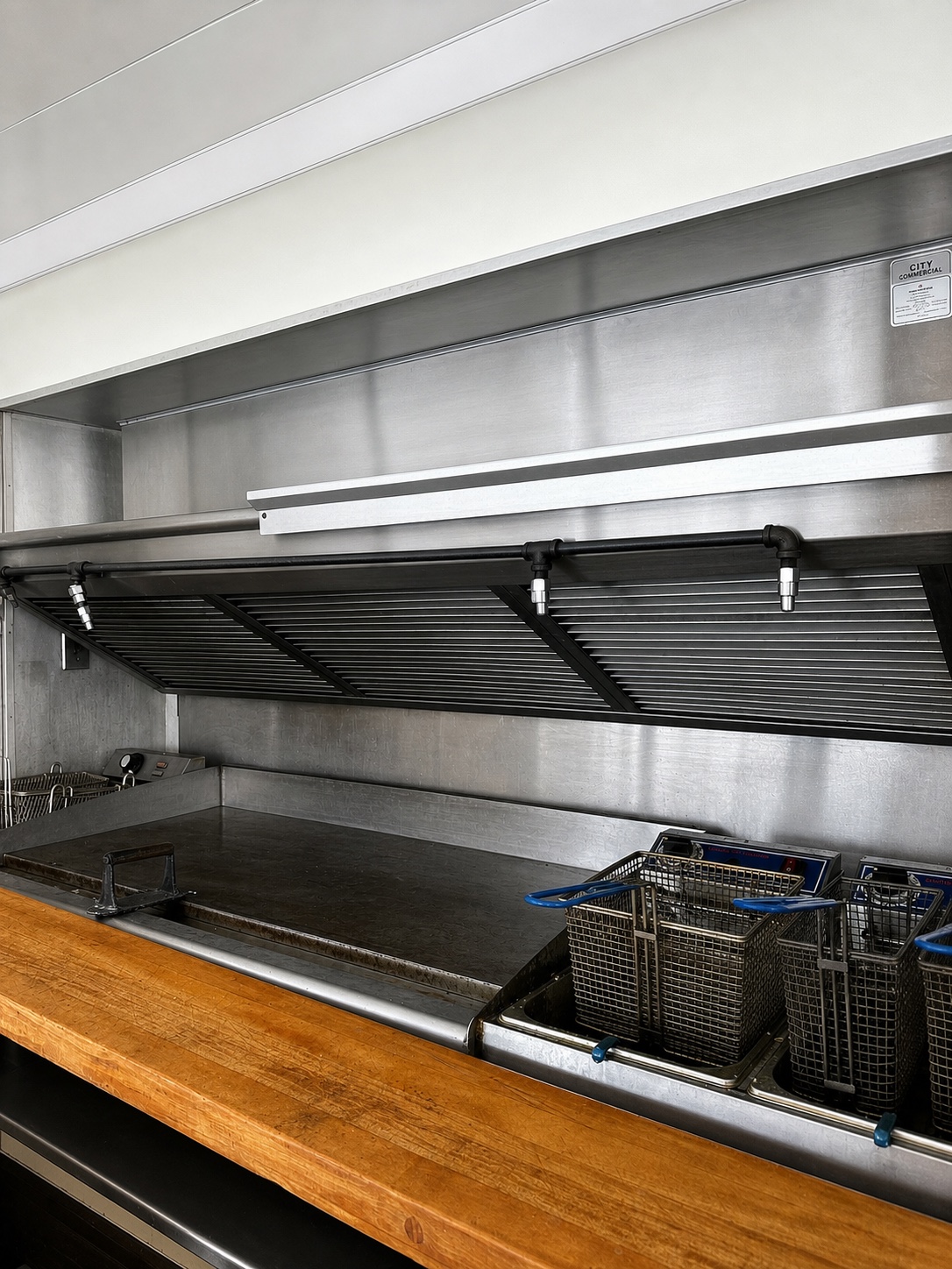 Commercial cooking line with griddle, fryers, and ventilation hood
