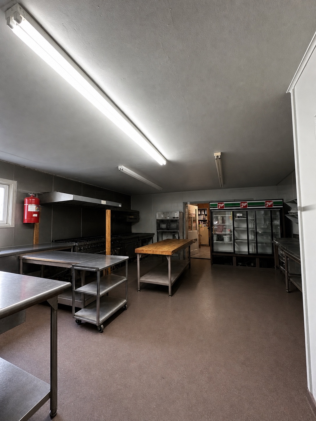 Full commercial kitchen with stainless prep tables, refrigeration, cookline, and ventilation
